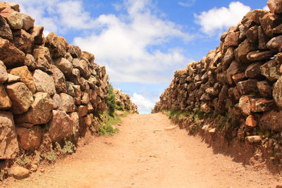 Empty footpath amidst stone wall against sky