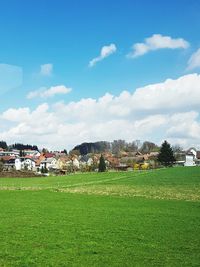 Scenic view of field by houses against sky