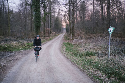 Rear view of man riding bicycle on road in forest