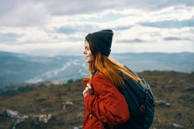 Side view of young woman looking at mountain against sky