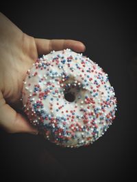 Cropped image of hand holding donut against black background