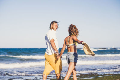 Couple walking at beach against sky