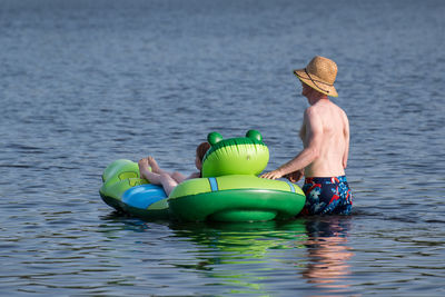 Shirtless man with daughter on inflatable raft in lake