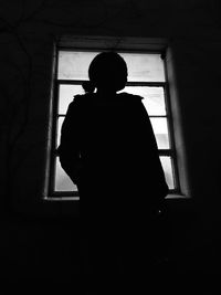 Silhouette woman looking through window at home