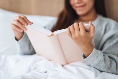 Midsection of woman sitting on bed at home