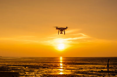 Low angle view of airplane flying over sea against sky during sunset