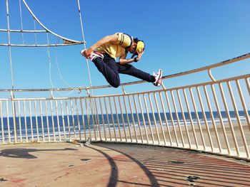 Low angle view of man jumping on railing against clear sky