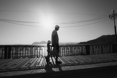 Rear view of man walking on bridge against sky