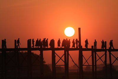 Silhouette monks and people on u bein bridge over river during sunset