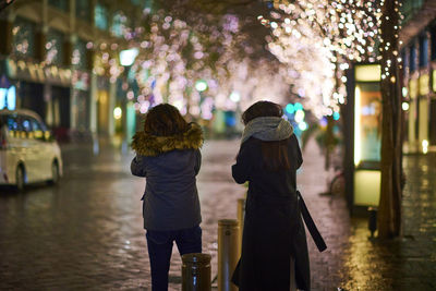 Rear view of women walking on illuminated street at night