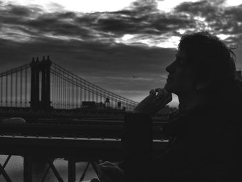 Person standing on bridge against cloudy sky