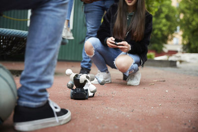 Low section of friends operating robots through smart phone during battle