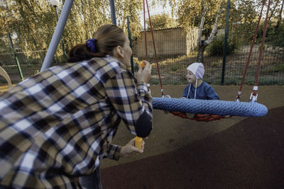 Cute little boy with down syndrome in a funny hat with his mother, swinging on a swing, soap bubbles