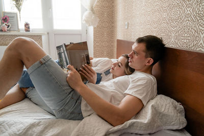 Friends using mobile phone while lying on bed at home