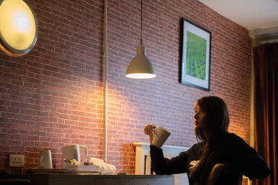 Woman looking at illuminated light fixture on brick wall