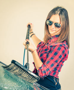 Woman wearing sunglasses washing car windshield in garage