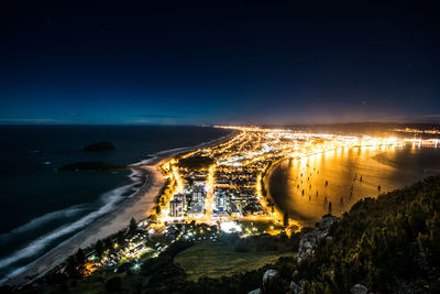 Illuminated city by sea against sky at night