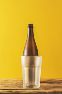 Close-up of empty glass bottle on table against yellow background