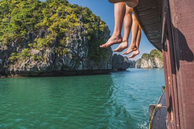 Low section of person sitting on rock by sea