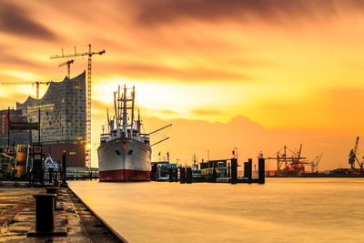 Cranes at commercial dock against sky during sunset