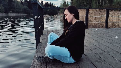 Woman sitting on pier over lake