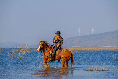 Man horse riding in lake against sky