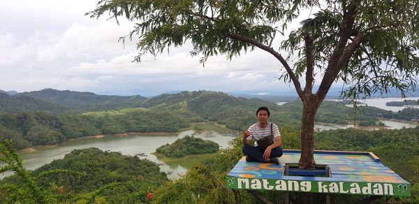 Full length of man sitting on mountain against sky