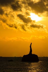 Silhouette statue by sea against orange sky