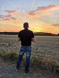 Rear view of man standing on field during sunset