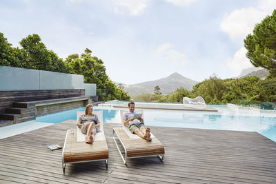 Heterosexual couple reclining on deck against swimming pool