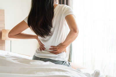 Rear view of woman sitting on bed at home