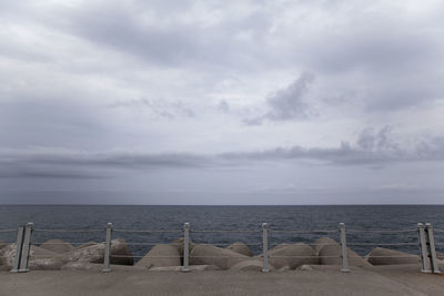 Tetrapod rocks by sea against cloudy sky