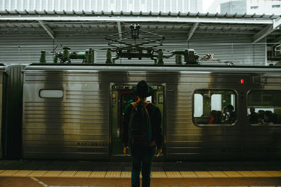 Rear view of man standing with backpack against train at railroad station