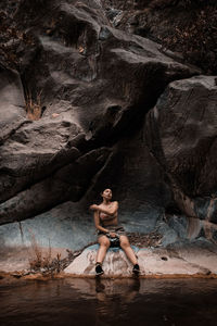 Full length of shirtless young woman standing on rock