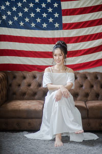 Portrait of smiling young woman sitting on sofa against american flag