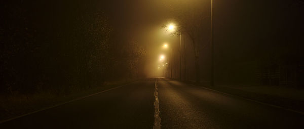 Empty road along trees at night