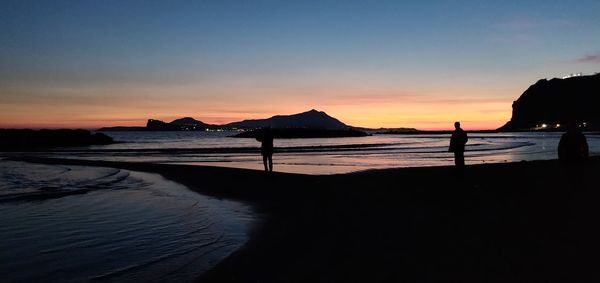 Silhouette people on beach against sky during sunset