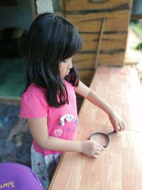 Cute girl standing holding magnifying glass on table