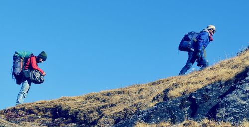 Low angle view of hikers on hill against clear blue sky