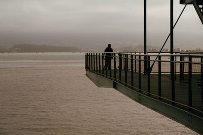 Silhouette man standing on bridge over sea against sky
