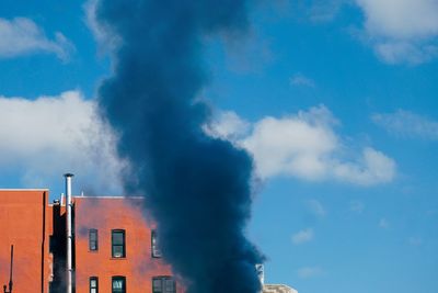 Low angle view of smoke emitting from chimney against blue sky