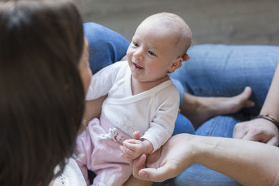 Woman holding smiling baby girl by friend sitting on floor at home