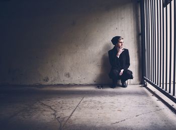 Man crouching and smoking against wall by gate