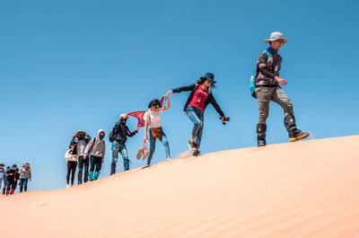 People walking on sand dune against clear sky