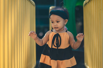 Thoughtful baby girl standing amidst yellow railings