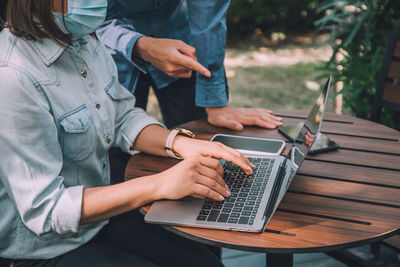 Midsection of businesswoman using laptop with colleague outdoors