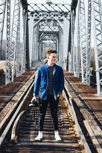 Young man holding camera standing at railway bridge