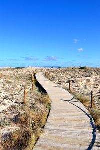 Walkway leading towards landscape against clear blue sky