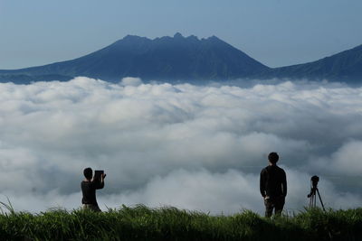 Two people overlooking clouds against mountains