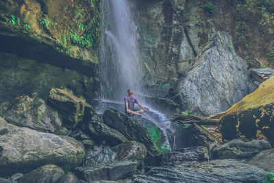Man sitting under waterfall in forest